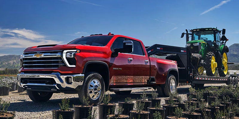 Chevrolet Silverado HD towing tractor on trailer outdoors